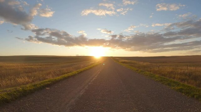 View from the front of a vehicle driving at sunset through open farmland
