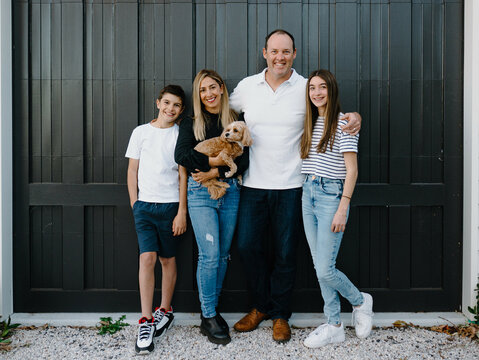 Happy family standing outside in front of black garage door with pet dog