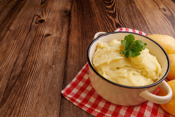  Bowl of mashed potatoes alongside whole potatoes and a red napkin, set on a brown wooden table, ideal for comforting and rustic food themes