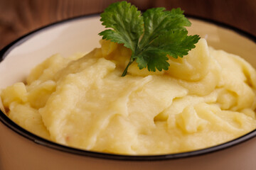 Close up of a bowl filled with freshly made mashed potatoes placed on a brown wooden table, showcasing the creamy texture and smooth consistency
