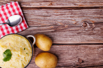 Bowl of mashed potatoes with whole potatoes, red checkered napkin, and spoon on an old wooden table, evoking a rustic Thanksgiving atmosphere