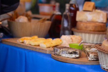 Horizontal photo. Cheese roll on wooden cutting board on blue table in street store. Farm food stall at city market. Cheese shop. Concept of buying dairy farm products. Tbilisoba harvest holiday. Fair