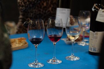 Horizontal photo. Three glasses with red and white wine on blue table. Food festival Tbilisoba. Day of city. Festive fair. Autumn harvest holiday. Wine counter, shop, store. Concept of drink, alcohol