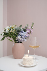 An Elegant Cake embellished with a Candle, glasse of wine and Beautiful Flowers displayed on a Table