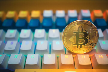 Golden Bitcoin coin placed on a vibrant gaming keyboard with colorful lighting, representing the...