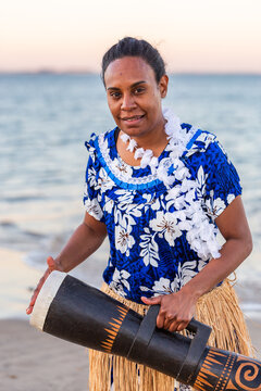 Torres Strait Island dance performer in traditional floral dress holding drum by ocean