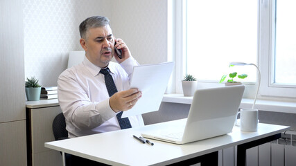 Man Working with Documents and Talking on Phone in Office