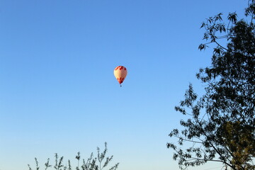A hot air balloon with a basket flies in the evening sky.