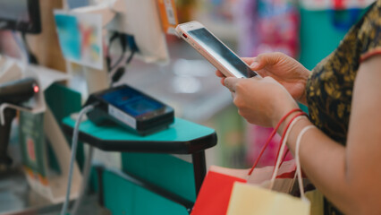 Shopper uses smartphone for payment at checkout counter, convenience of digital transactions in everyday shopping