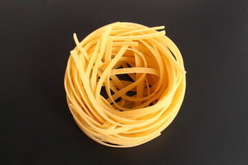 One twisted spaghetti nest lies on a black background.