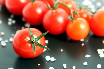 Red fresh cherry tomatoes lie on a black background.