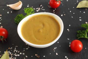 A white bowl of mustard stands on a black background.