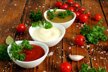 There are three bowls of mayonnaise, ketchup and mustard on a wooden table.