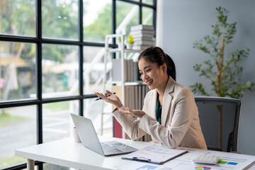 A woman is sitting at a desk with a laptop and a pen