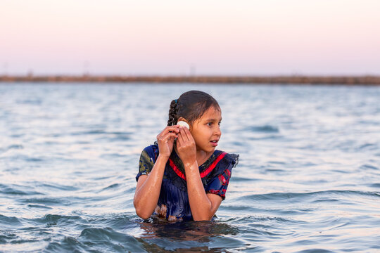 Torres Strait Islander child listening to shell in ocean water at dusk
