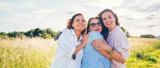 Portrait of three cheerful smiling women embracing during outdoor walking. They looking at the camera. Woman friendship, relations, and happiness concept image.