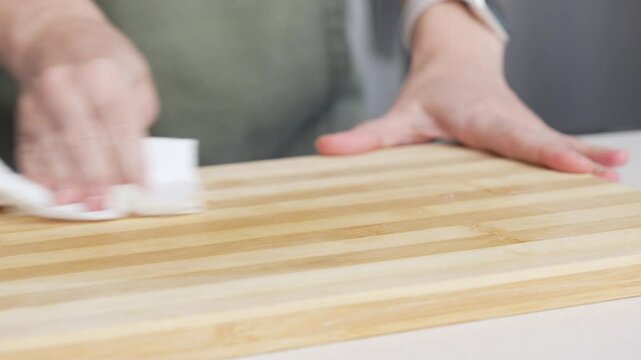 Hands wiping the wooden cutting board with a paper towel. Woman in the Kitchen Cleaning the Countertop, Preparing for Cooking Food.