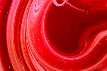 Beautiful abstraction of liquid red and pink paints in slow blending flow mixing together gently.