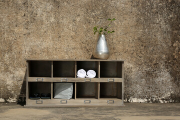 A compact wooden shelf adorned with a sleek silver vase and minimal decor rests against a weathered stone wall.