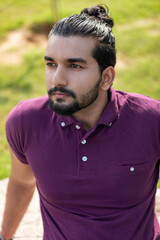 Close-up portrait of a confident, handsome, bearded Asian-Indian man with a ponytail. He's gazing...