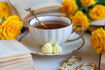 On the white table there is hot tea, cakes and delicate roses.
