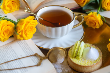 On the white table there is hot tea, cakes and delicate roses.
