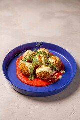 Deep fried arancini balls served on blue plate with sauce and herbs