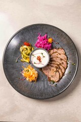 Sliced roast beef with spices and side dish on black plate