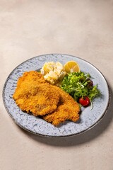 Wiener schnitzel lying on a plate with potato salad and green salad