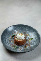Chocolate lava cake being decorated with vanilla ice cream and pistachios on dark plate