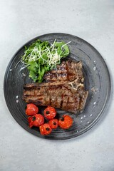 Grilled t-bone steak served on plate with tomatoes and arugula salad