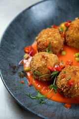 Delicious deep fried arancini rice balls served on grey plate with red sauce and garnish