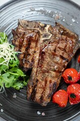 Grilled t-bone steak served on plate with tomatoes and arugula
