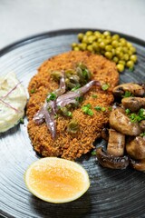 Breaded escalope with mushrooms, green peas and lemon on plate