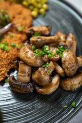 Close up of sauteed mushrooms garnished with chives on a black plate