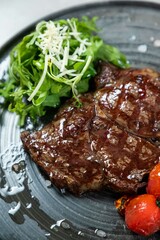 Grilled ribeye steak with salad and roasted tomatoes on black plate