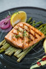 Grilled salmon fillet lying on asparagus with lemon and spices on black plate