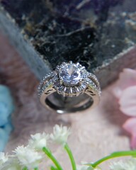 Sparkling silver ring resting on stone with flowers
