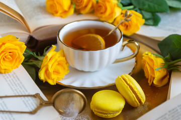 On the white table there is hot tea, cakes and delicate roses.