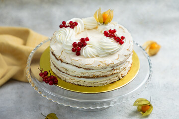 Delicious meringue cake decorated with redcurrant and cream standing on glass cake stand