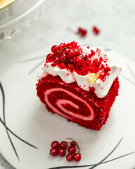 Red velvet swiss roll cake lying on white plate decorated with redcurrant and cream
