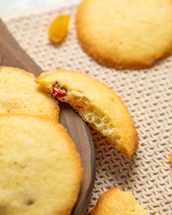 Close-up of delicious round cookies with candied fruit on a wooden board and a beige napkin
