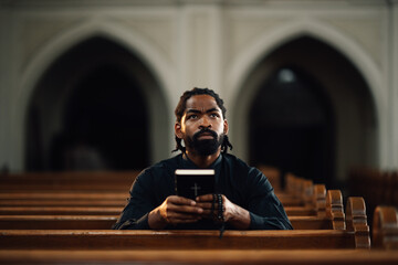 Priest praying in church holding bible looking up