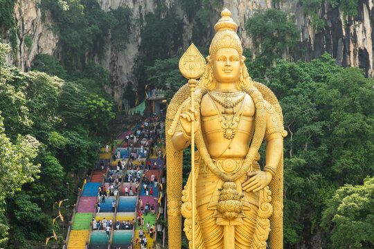 Batu Caves Hindu Temple, Selangor, Malaysia. Golden statue of Lord Murugan with tourists on colorful staircase leading to Batu cave complex, Kuala Lumpur. Travel Hinduism landmark in Asia