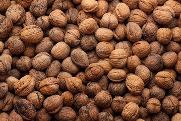 Close-up of a large pile of whole walnuts in their shells, showing a natural and organic texture.