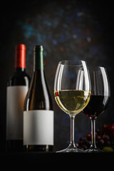 A dark, elegant still life of White and Red wine in a glass with wine bottles and fresh grapes in the background. Perfect for wine-themed compositions