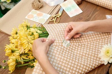 Close up of female hands putting on sticker on rustic style bouquet composition of yellow flowers...