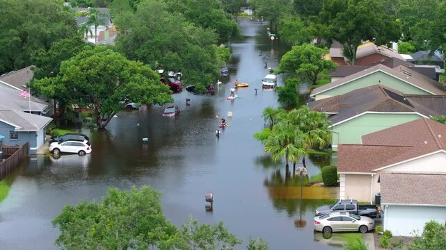 People kayaking on flooded street in Sarasota, Florida after hurricane Debby torrential rainfall drowned rural homes in residential area.