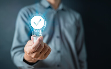 inspiration, innovation, tech, idea, lightbulb, creativity, imagination, intelligence, invention, solution. A man is holding a light bulb with a check mark on it. Concept of innovation and progress.