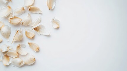 Close-up of garlic cloves peeled from a whole bulb, scattered artistically on a clean white background, creating a fresh, minimal look.